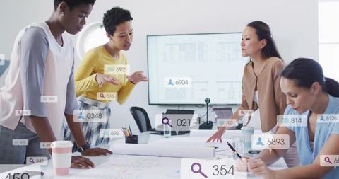 Collaborating women reviewing architectural blueprints and analytics in modern office
