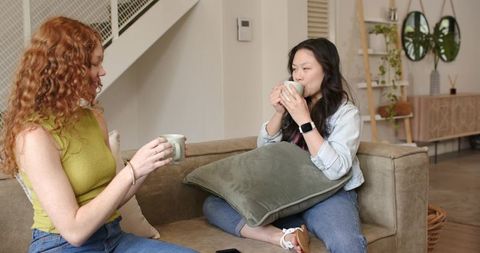 Female friends enjoying coffee and conversation on cozy living room sofa