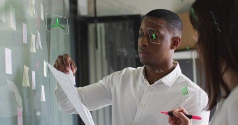 Man placing paper on glass planning board during collaborative brainstorming session