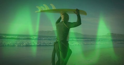 Surfer holding board under vibrant green light on ocean beach