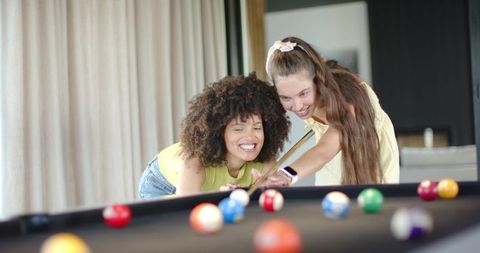 Women playing pool together leaning over black-felt table enjoying casual game night