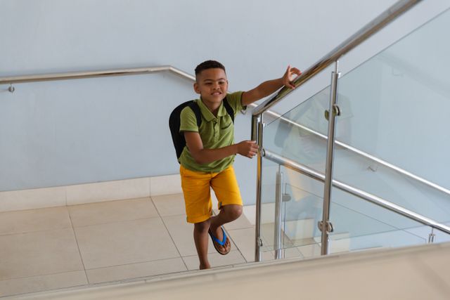 High angle view of smiling african american elementary schoolboy climbing steps in school building. unaltered, childhood, education and school concept.