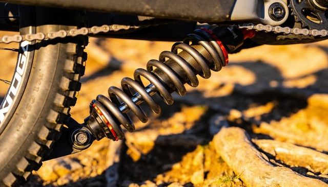 Mountain bike rear coil shock compressing on rocky trail during golden hour