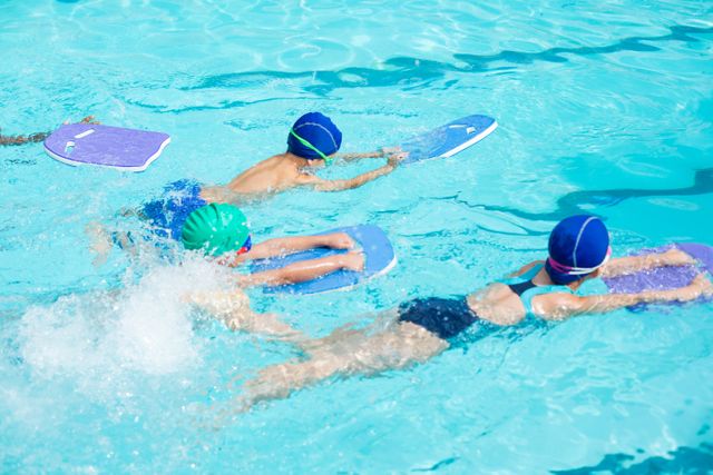 Children practicing swimming with kickboards in a pool, ideal for illustrating swim classes, aquatic training, children's sports activities, and summer fun. Useful for educational materials, sports programs, and health and fitness promotions.