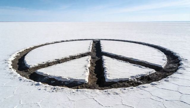 Peace sign carving on salt flat revealing dark soil, geometric circle land art on playa