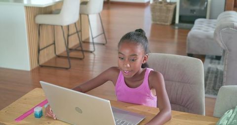 African american teen studying on laptop at home kitchen table with focused expression