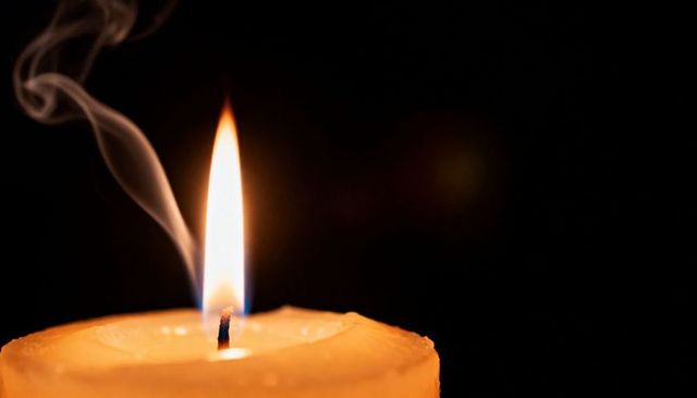 Single Burning Candle Casting Warm Amber Glow with Flickering Flame and Wisps of Smoke