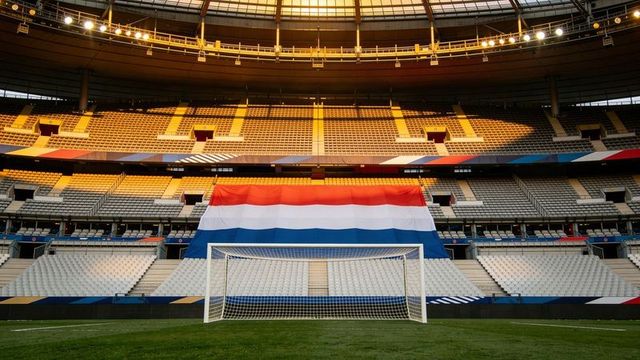 Empty soccer goal facing giant red white blue flag draped over stadium stands