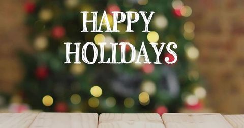 Happy holidays text over blurred christmas tree with bokeh lights on wooden tabletop