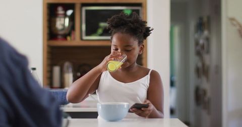 Girl Drinking Juice While Using Smartphone in Bright Kitchen