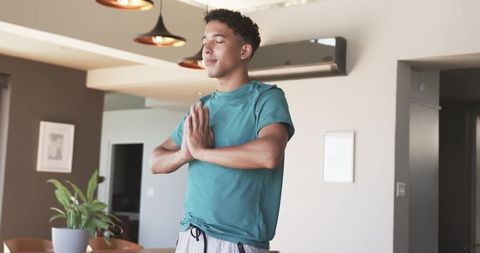 Young man practicing meditation at home with palms together in modern minimalist interior