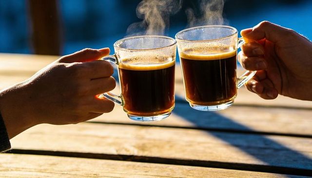 Clinking glass coffee mugs on sunlit wooden deck, steam rising, morning toast, cozy hands