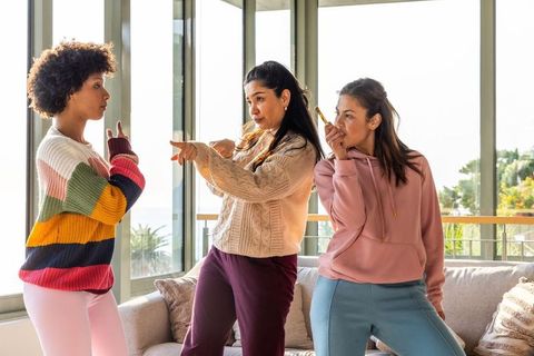 Multiracial women gesturing, joking, and debating in sunlit living room with balcony view