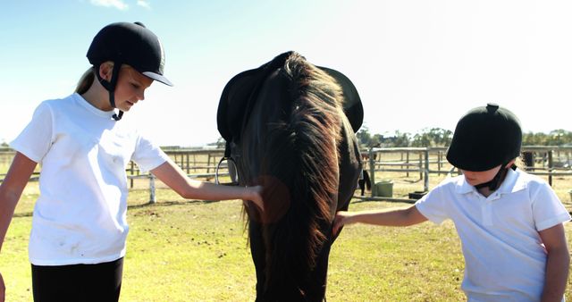 Two young Caucasian girls in equestrian attire are grooming a horse outdoors, with copy space. They are learning about horse care and bonding with the animal through this hands-on activity.
