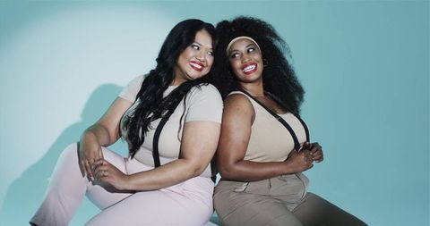 Confident plus size women sitting back to back smiling