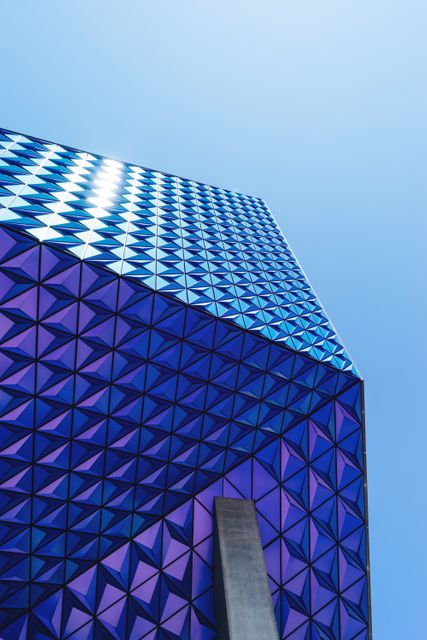 Triangular glass facade of a modern building against a clear blue sky. Ideal for architectural design concepts, urban planning presentations, contemporary structures, and cityscape visuals.