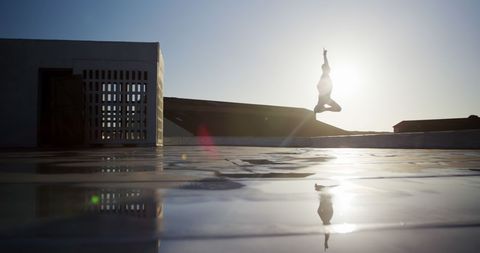 Silhouette of male dancer jumping on sunny rooftop