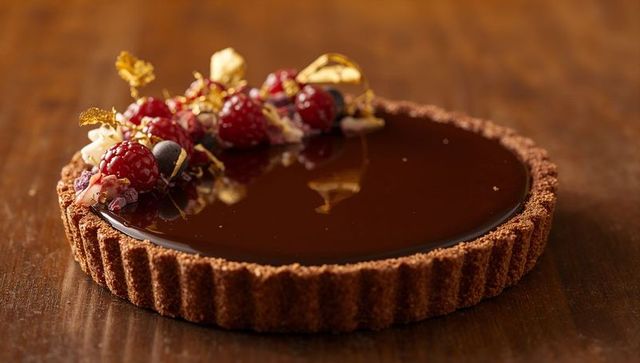 Glossy chocolate ganache tart garnished with raspberries, blueberries and gold leaf