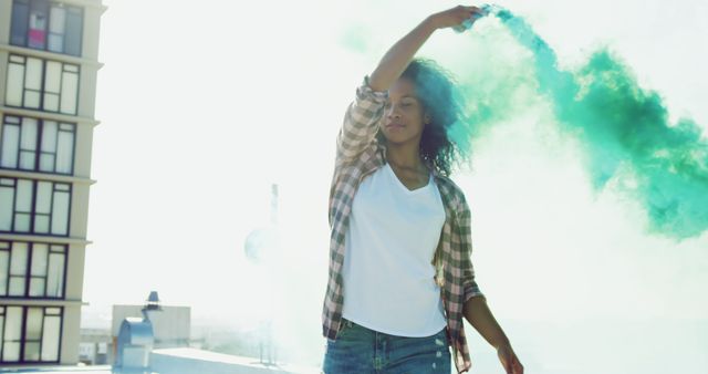 Young biracial woman enjoys a sunny day outdoors, with copy space. She exudes freedom and joy while holding a colorful smoke flare.