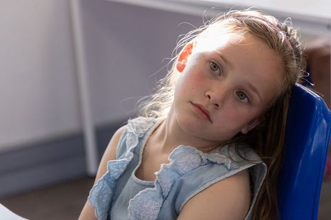 Pensive young girl sitting in classroom, gazing away in soft natural light, quiet portrait