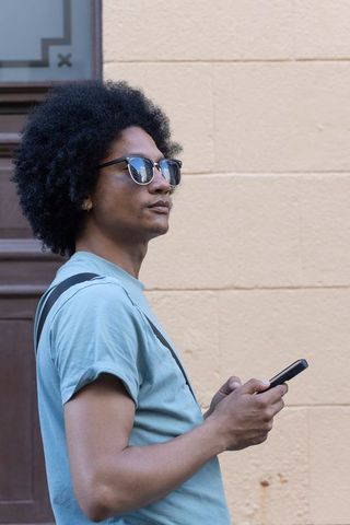 African man checking smartphone wearing sunglasses and shoulder strap on urban street