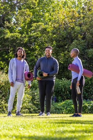 African american friends holding yoga mats and smiling in sunlit park