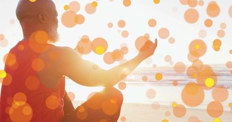 Elder man meditating on beach at sunrise with warm orange bokeh and peaceful backlight