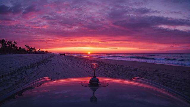 Car hood reflecting sunset over palm beach at twilight with tire tracks and silhouettes