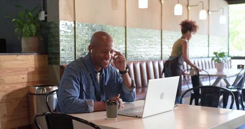 African american man joining video call at modern cafe with laptop and coffee, denim shirt
