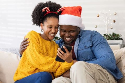 African American Couple Sharing Festive Smartphone Laughs Wearing Santa Hat