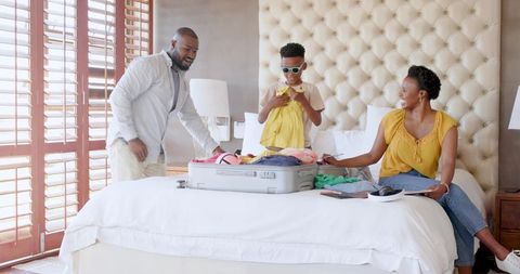 African American Family Packing Suitcase on Bed in Sunlit Hotel Suite Preparing for Trip