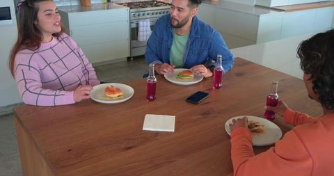 Diverse friends enjoying casual burger lunch in modern white kitchen with wooden table