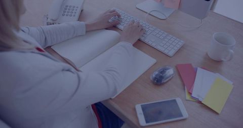 Professional Woman Typing at Modern Workspace with Notebook and Smartphone