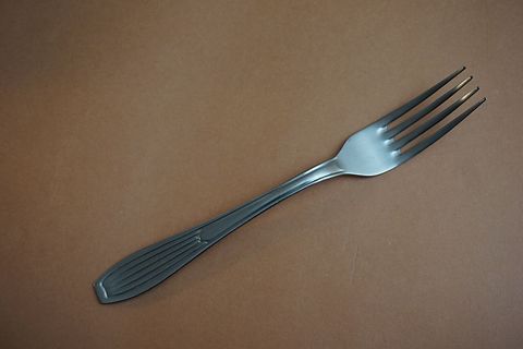 Stainless Steel Dinner Fork Lying on Warm Brown Surface with Classic Ribbed Handle