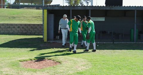 Baseball team gathering with coach near dugout planning strategy on sunny community field
