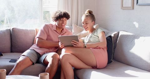 Diverse Couple Relaxing on Sofa Using Tablet in Bright Living Room