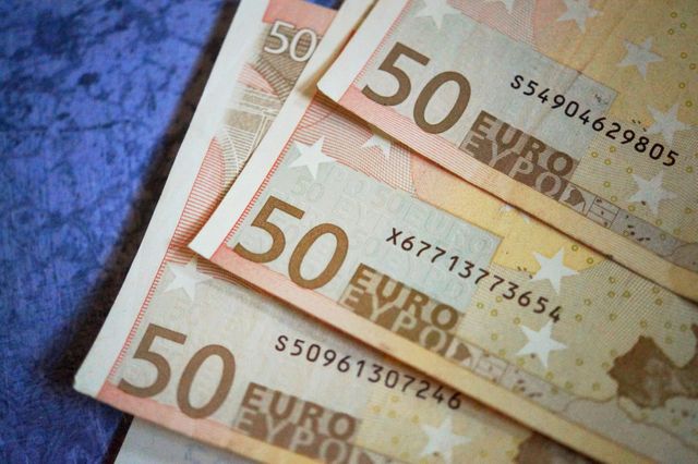 Colorful fifty-euro banknotes are laid out showing the numbers and designs of the currency, placed on a blue textured surface. This close-up view is ideal for use in financial articles, business presentations, marketing materials for banks or currency exchange services, and educational purposes related to European finances or economy.