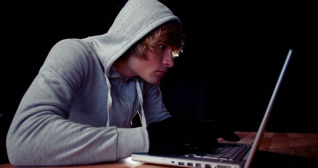 Focused caucasian man in hoodie using laptop with copy space. Technology, connection, communication and lifestyle concept, unaltered.