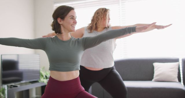 Two women with diverse body types practicing yoga poses together in a bright living room. Perfect for illustrating home fitness routines, promoting healthy lifestyles, diversity in fitness, and yoga practices.