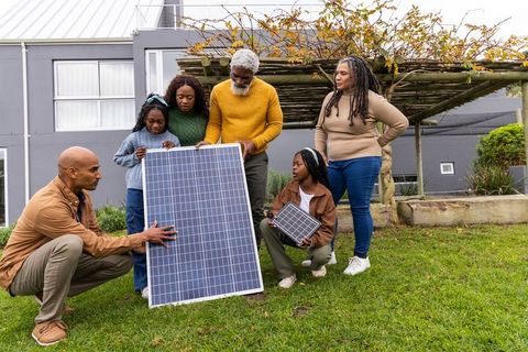 African american multigenerational family inspecting solar panel and mini module in backyard