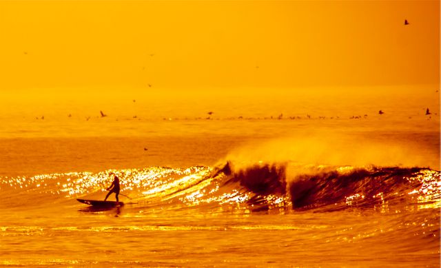 view of person surfboarding in the waves in the sea during sunset. sports and competition concept