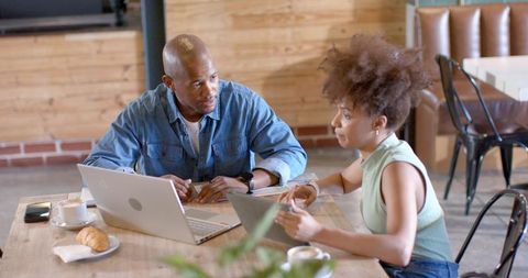 Young professionals collaborating on laptops and tablets while sharing coffee and croissant