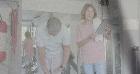 Mature couple exercising at home gym man catching breath woman checking tablet