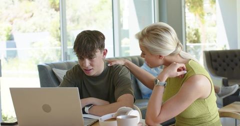 Parent guiding teen working on laptop at home — mentoring, study support, family learning