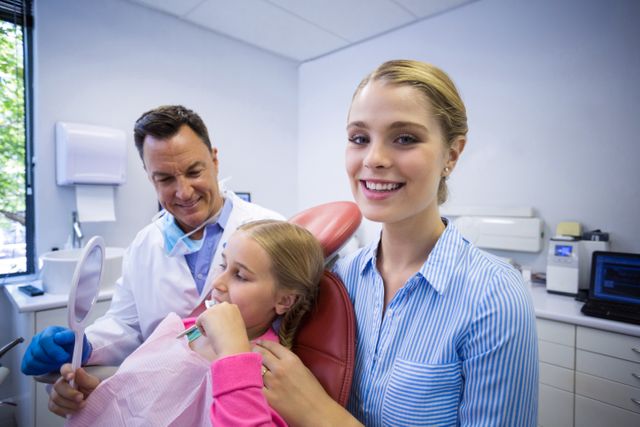 Dentist assisting a young patient in brushing teeth while a dental assistant smiles at the camera. Useful for illustrating dental care, pediatric dentistry, and healthcare services. Ideal for websites, brochures, and educational materials promoting oral health and dental hygiene.