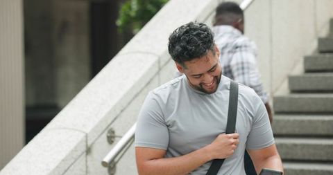 Commuter checking phone on urban stair landing while carrying crossbody bag