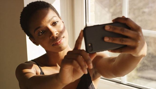 Sunlit woman taking selfie by window with smartphone, natural light intimate portrait
