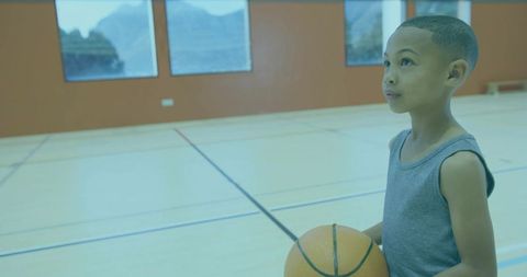 Young Boy Holding Basketball on Indoor Court