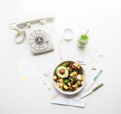 Serving brunch skillet with avocado and potatoes beside retro rotary telephone flat lay