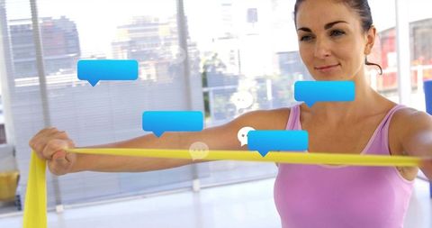 Woman pulling resistance band while receiving digital chat notifications, fitness concept